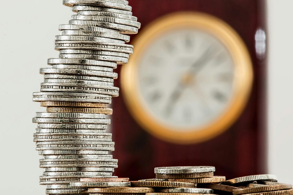 A close-up image of stacked coins with a blurred clock, symbolizing time and money relationship. The Power of Compounding