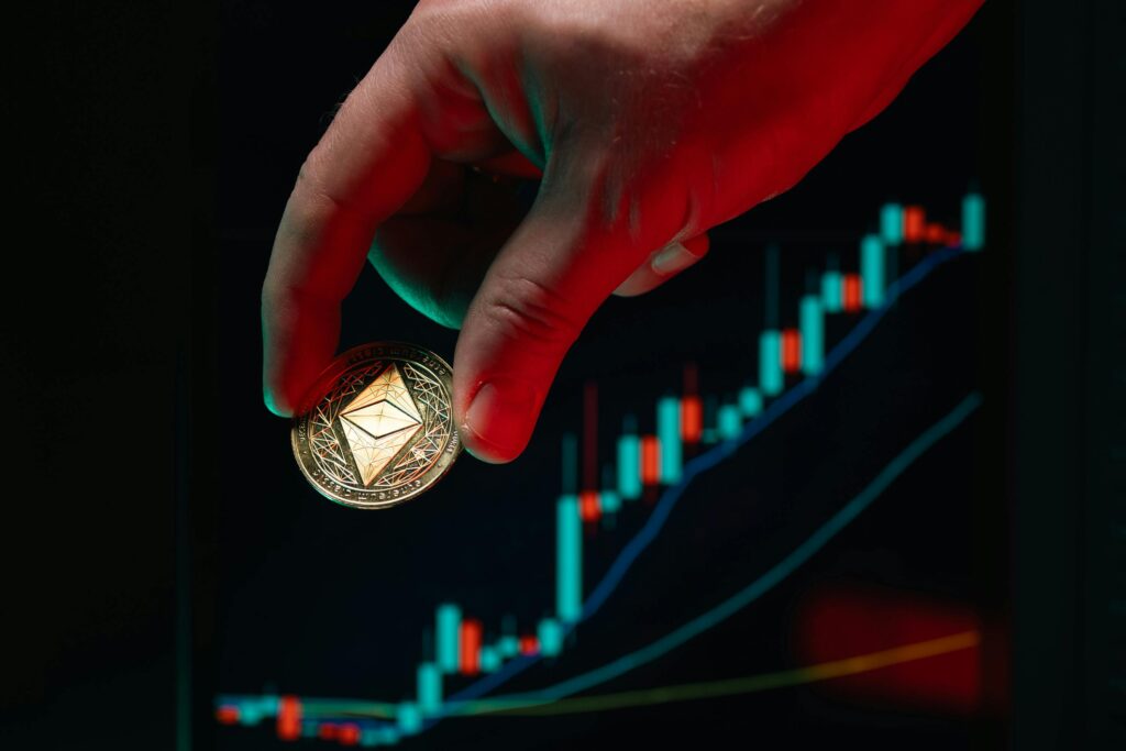 A hand holding an Ethereum coin against a rising stock market graph, symbolizing cryptocurrency growth. Invest in Gold Now?