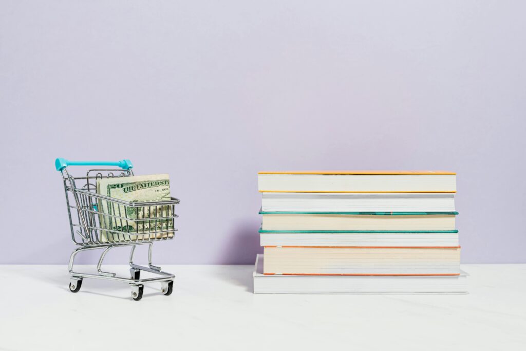 A shopping cart with dollar bills next to a stack of textbooks on a light background. Best Money Books