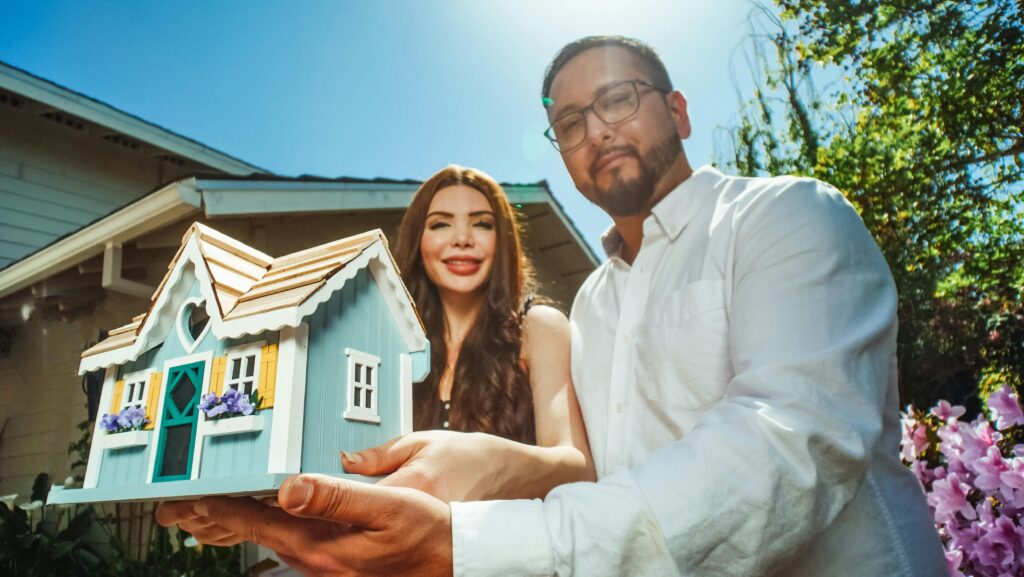 Happy couple proudly holding a miniature house symbolizing new homeownership. Housing Guide: Is Renting or Buying Better