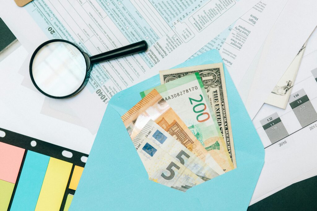 Close-up of tax documents and mixed currency in a blue envelope with a magnifying glass, perfect for financial analysis concepts. Envelope System Budgeting