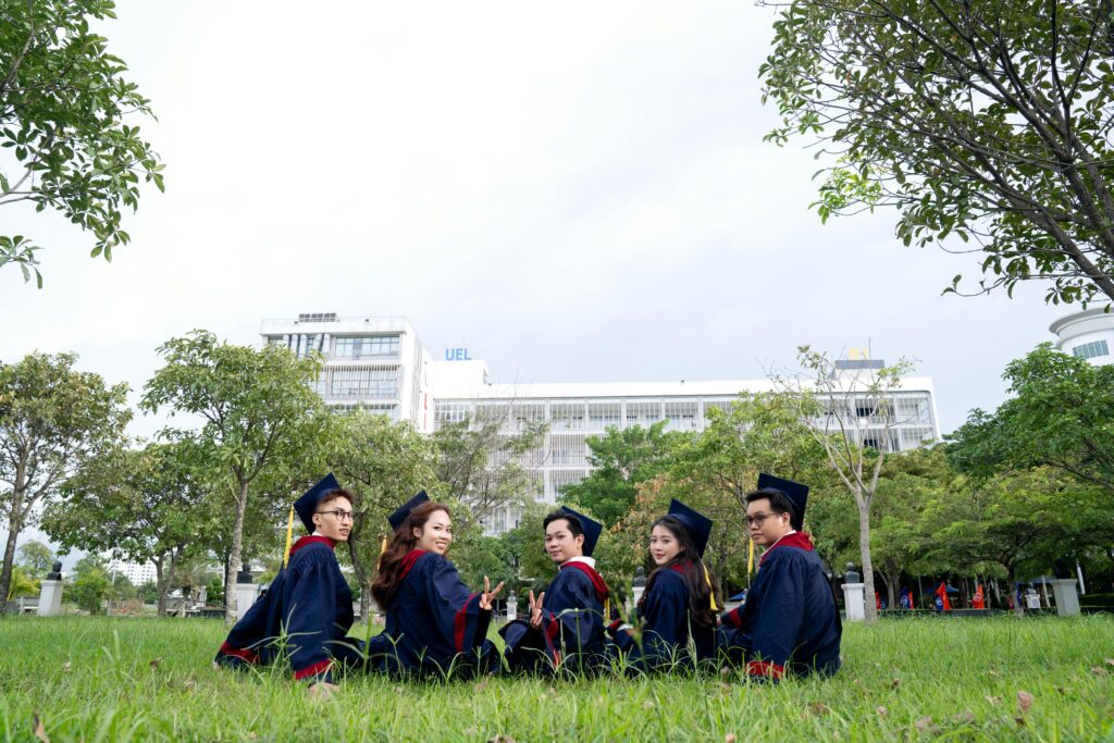 Group of five university graduates celebrating outdoors in regalia, sitting with a campus backdrop. Save for Child’s Education