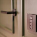 A smart light switch on a wall next to a modern door handle, emphasizing home automation.