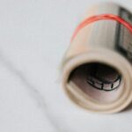 Rolled-up US dollar bills secured with a red rubber band on a marble surface, symbolizing finance and savings.
