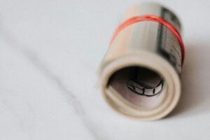 Rolled-up US dollar bills secured with a red rubber band on a marble surface, symbolizing finance and savings.