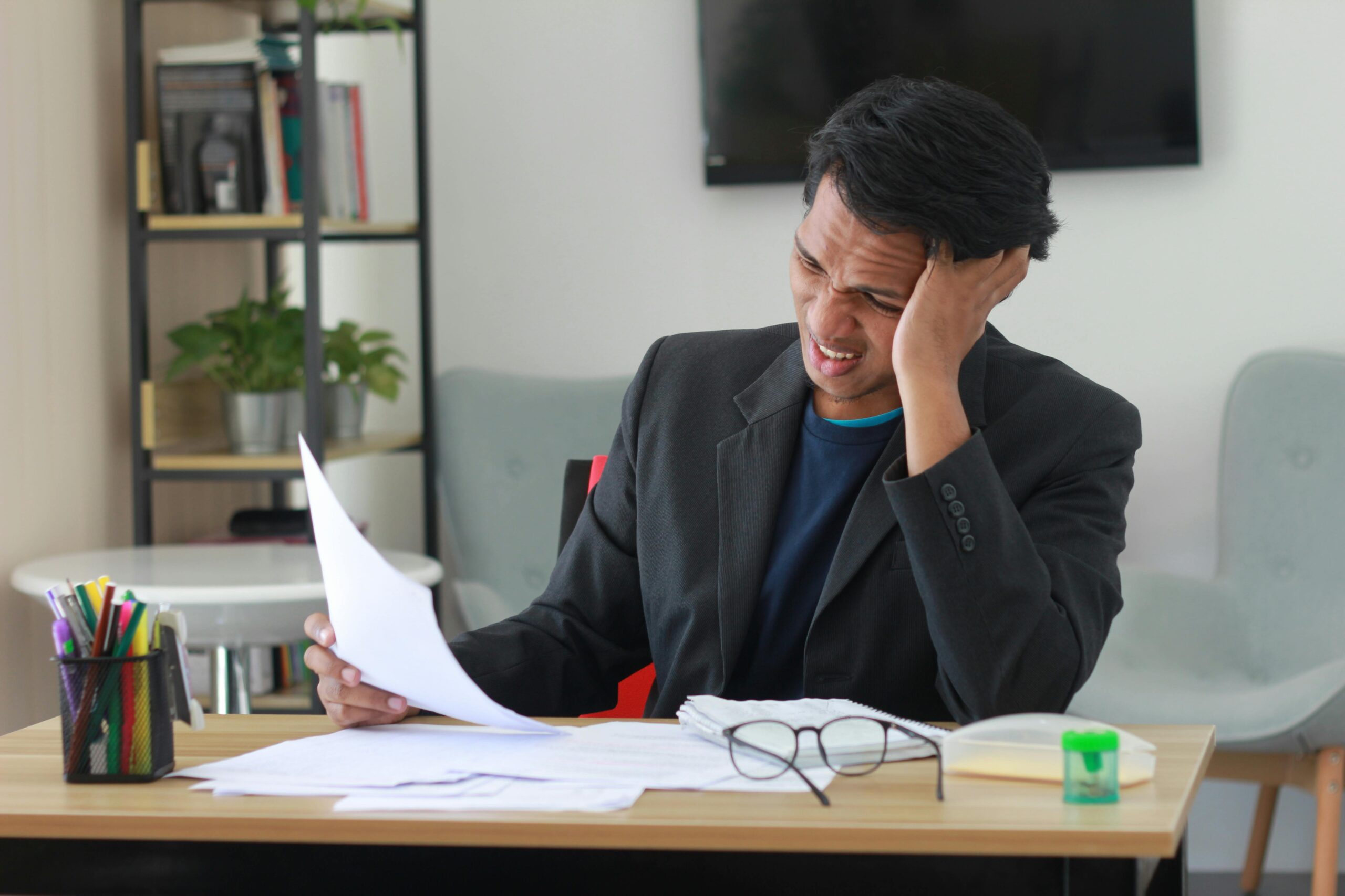 A businessman in an office experiencing stress while reviewing documents.