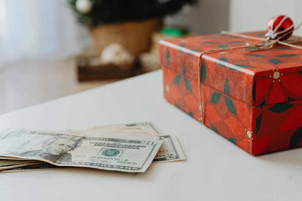 Red festive gift box with US dollar bills on a table, ideal for holiday-themed uses. Debt-Free Holiday Plan