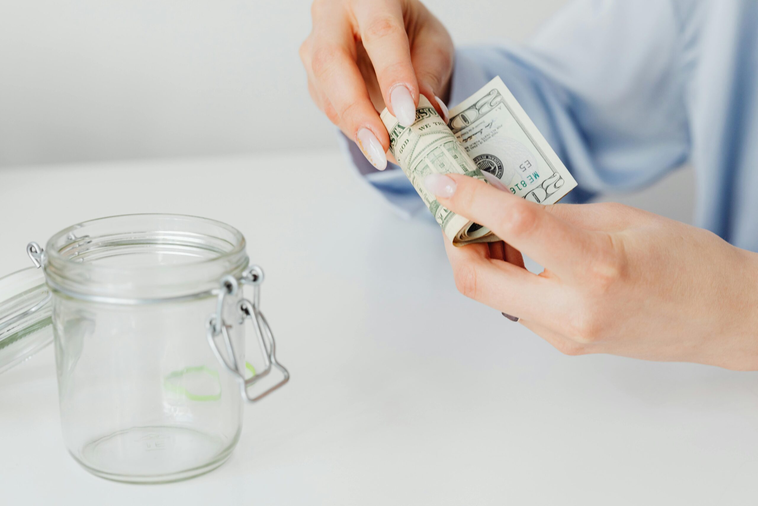 Woman rolling dollar bills beside a glass jar, symbolizing savings or financial planning.